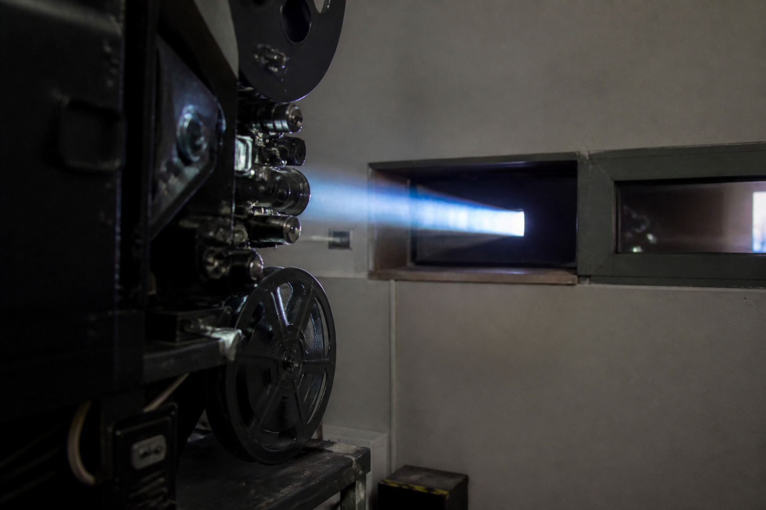 Proyector de cine de 35 milímetros en una cabina, con el haz de luz atravesando la ventanilla hacia la sala